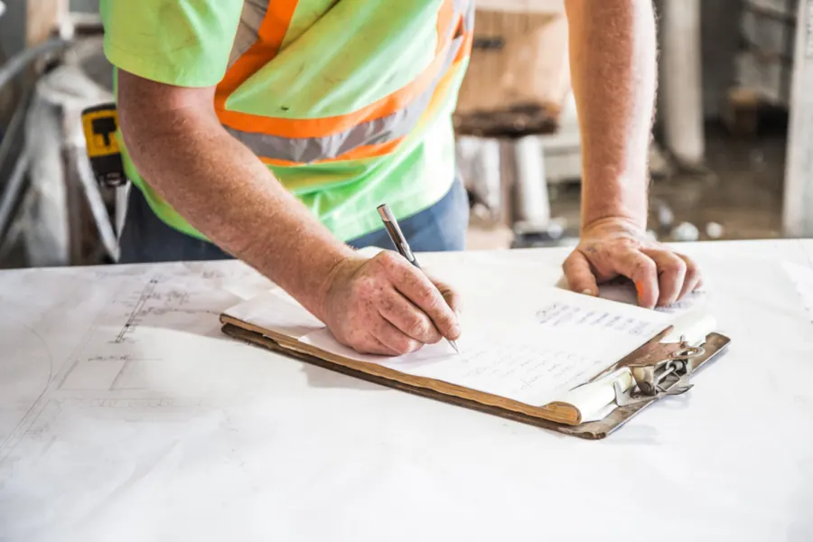 Site worker writing notes on a clipboard over construction drawings