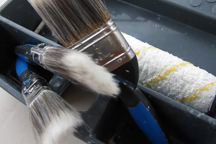 Paint brushes and a roller resting in a paint tray