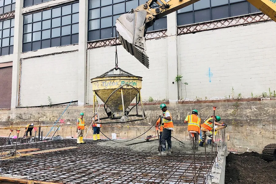 Crew pouring concrete over a reinforcing steel grid to form a structural slab