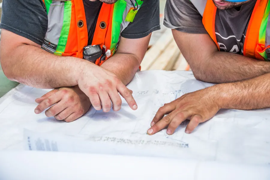 Two workers in high-visibility vests pointing at building drawings on a table