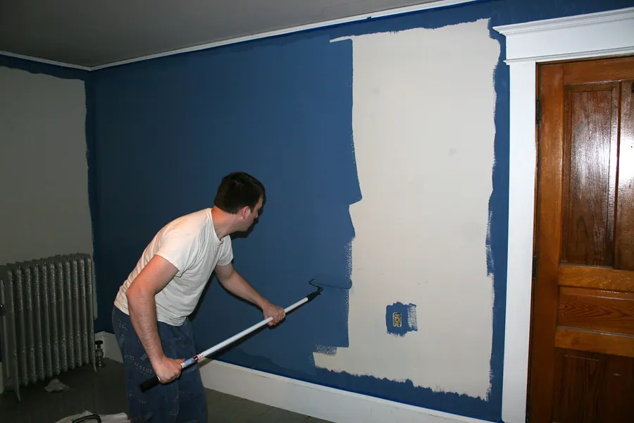 Painter rolling a coat of blue paint onto an interior wall